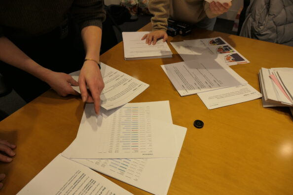 Three BetaNYC staff members spread out papers on a wooden table.